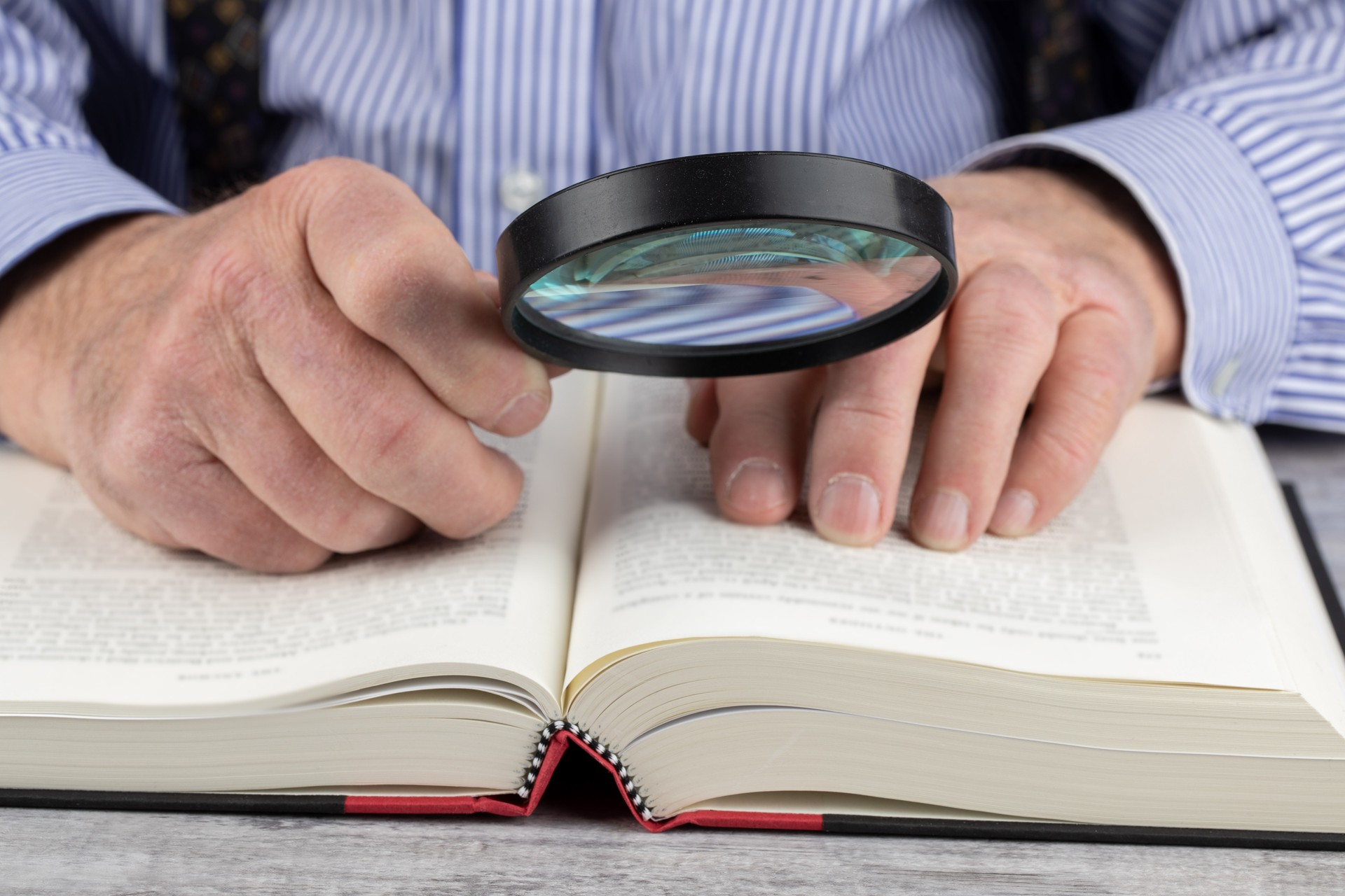 close up view of an elderly man using a magnifying glass to read a book